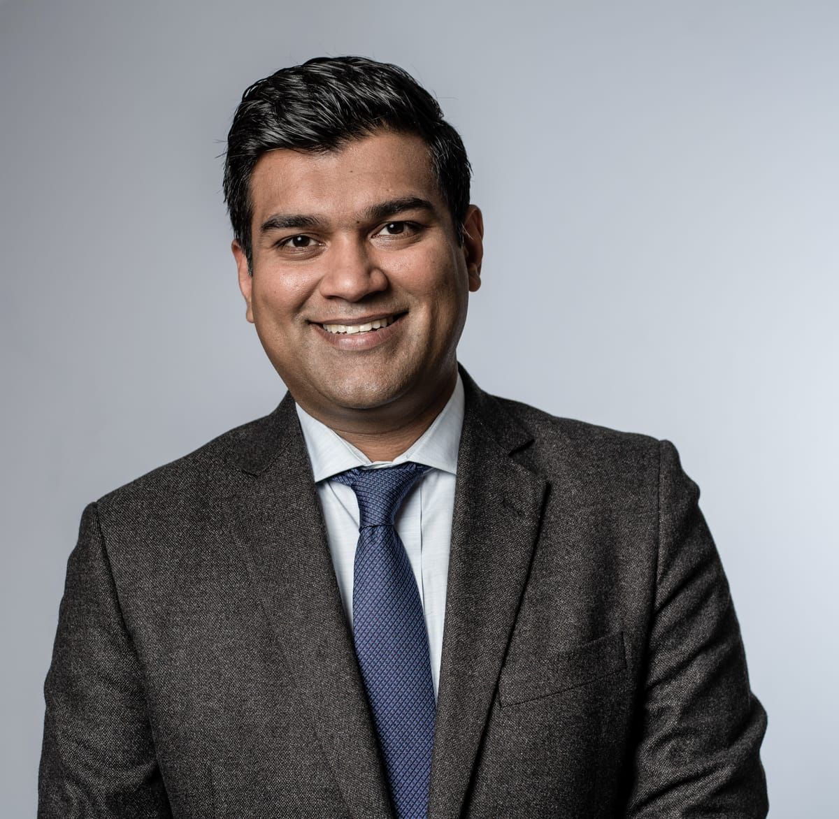 Corporate portrait of a smiling man in a charcoal suit and blue tie
